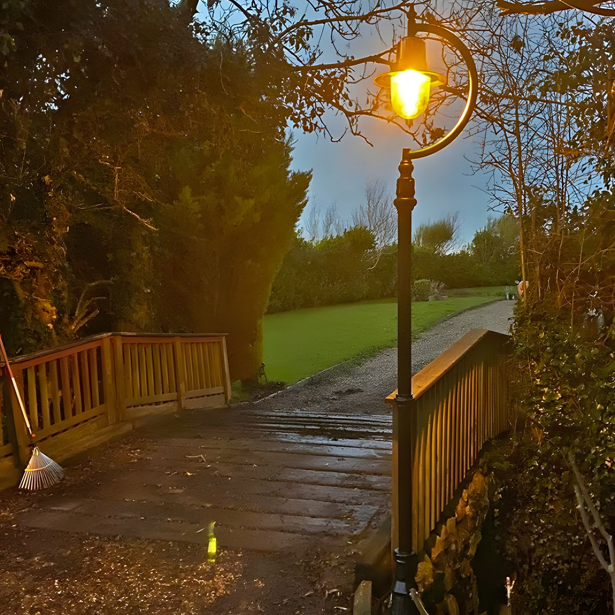 Vintage Cast Iron Lamp Post 2.8m in black with a curved goose neck arm and teardrop shade, illuminated on a wooden bridge beside a garden path at dusk.