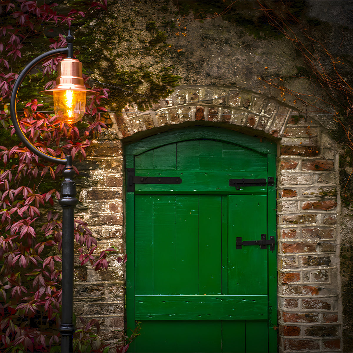 Vintage Cast Iron Lamp Post 2.5m with curved goose neck arm and copper teardrop shade, lit against a brick wall and green door in a garden setting.