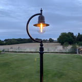 Vintage Cast Iron Lamp Post 2.5m in black with curved gooseneck arm, teardrop shade and glass dome, lit outdoors on a lawn beside white fencing and open fields.