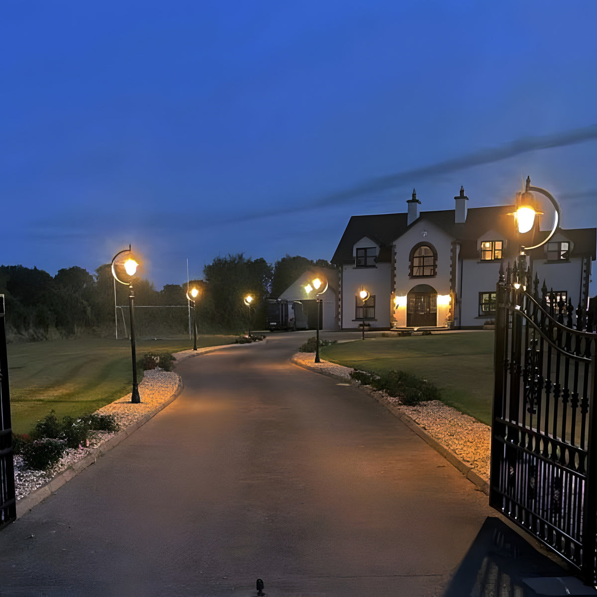 Vintage cast iron lamp posts, 2.5m black gooseneck design with teardrop shades, lighting a driveway leading to a house at dusk.