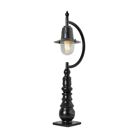 Small vintage black cast iron pedestal post light with a curved gooseneck arm, teardrop glass shade, visible filament bulb, and decorative base with mounting plate.