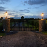 Large Vintage Cast Iron Pillar Light in black, gooseneck curve with teardrop shade, illuminated atop stone gate piers at dusk.