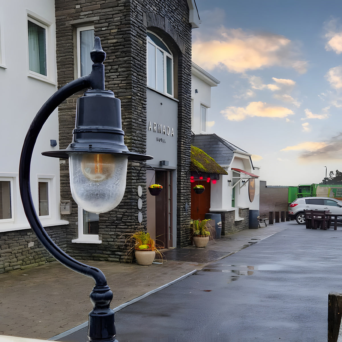 Large Vintage Cast Iron Pillar Light in black with gooseneck curve and teardrop shade, mounted on a stone pier outside a building entrance.