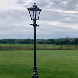 Victorian Manor 3m cast iron lamp post in black with hexagonal lantern head and glass panels, shown outdoors on a lawn beside a field.