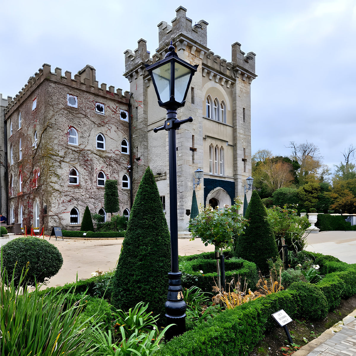 Victorian Manor Cast Iron Lamp Post 3m in black, slim column with single glass lantern head, positioned in a formal garden setting before a stone castle-style building.