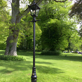Victorian Manor 3m cast iron lamp post in black with a slim decorative column and single lantern head, shown outdoors on a lawn beside mature trees.