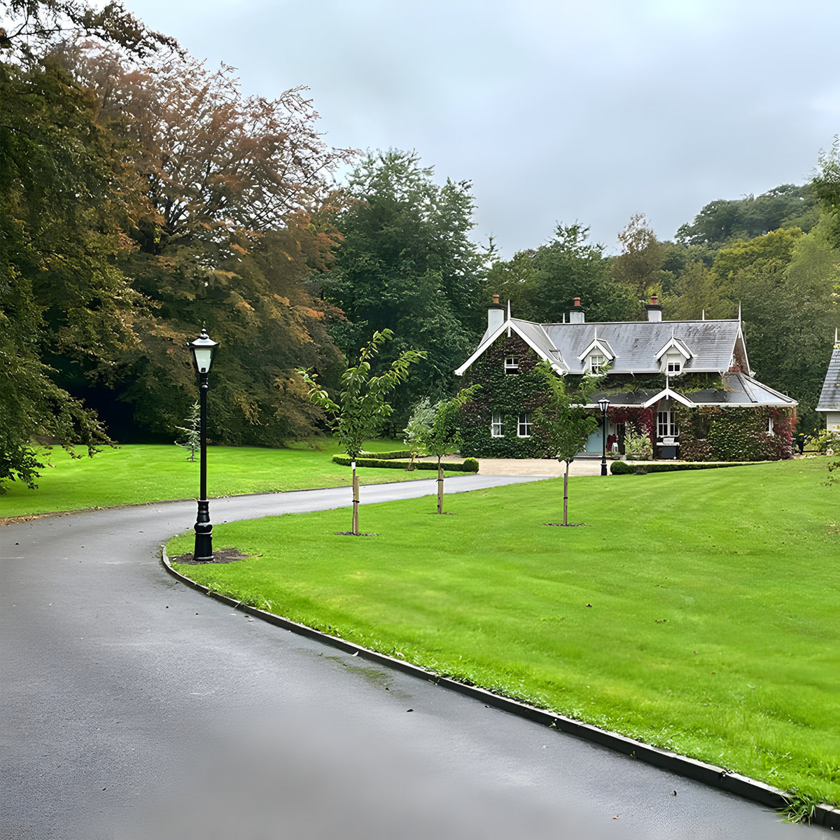 Victorian Manor Cast Iron Lamp Post 3m in black, slim unornamented column with lantern head, installed along a driveway beside a lawn and traditional house.