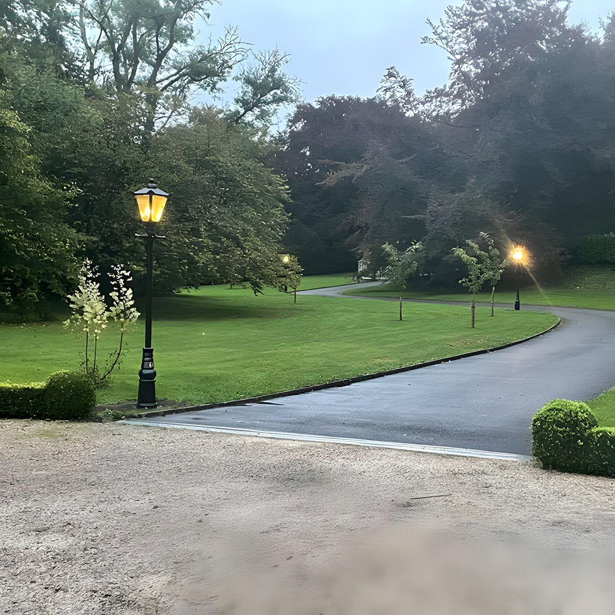Victorian Manor 3m cast iron lamp post in black with lantern-style glass head, illuminated on a garden driveway lined with lawn and trees.