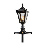 Victorian Manor cast iron lamp post in black with a hexagonal lantern head, decorative finial, cross arms and clear polycarbonate glazing around a lit E27 bulb, shown against a plain white background.