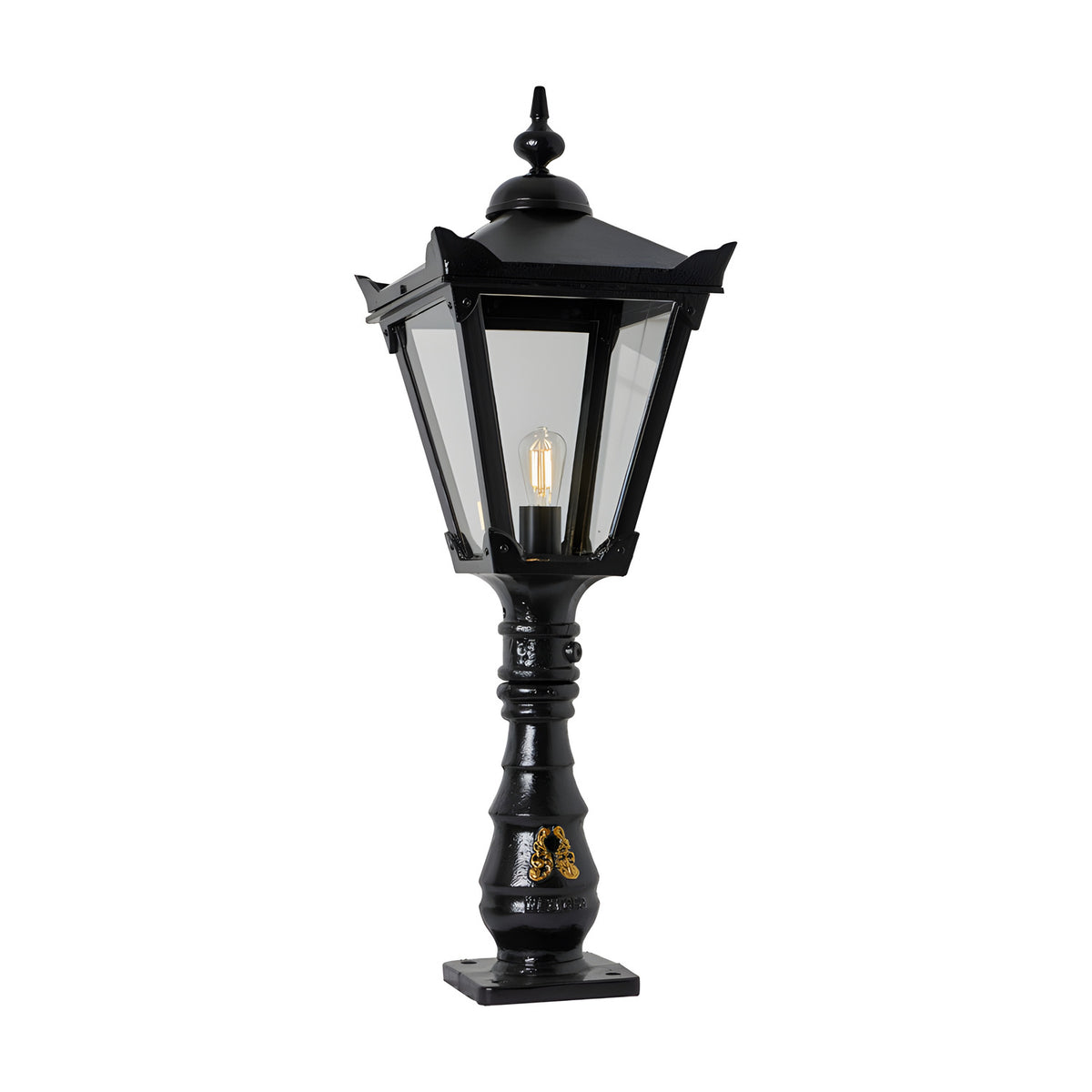 Black cast iron Victorian Manor pedestal post light with square lantern head, clear glass panels, decorative finial, and slim ornamented column on a square base.