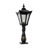 Black cast iron Victorian Manor pedestal post light with square lantern head, clear glass panels, decorative finial, and slim ornamented column on a square base.