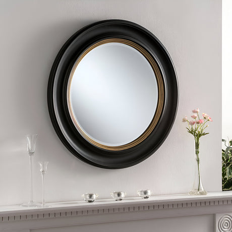 The Hamilton Circle Wall Mirror Black/Gold - 66cm is displayed on a white wall above a shelf, which enhances its contemporary style with two glass vases, pink flowers, and three small metallic bowls.