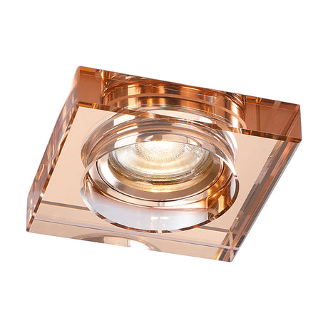 Square crystal downlight rim in rose gold with a deep faceted profile, shown with the lampholder and lit bulb fitted, on a plain white background.