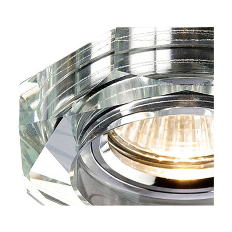 Close-up of the Crystal Downlight Rim, a clear octagonal crystal trim with angled faceted edges surrounding a lit halogen bulb, 90mm diameter for a 62mm cut-out.