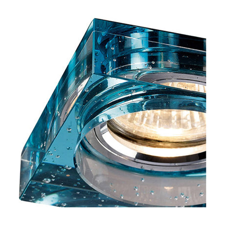 Close-up of a square crystal downlight rim in aqua blue with a bubbled, rippled surface, 90mm face, shown lit with a recessed bulb visible through the centre.
