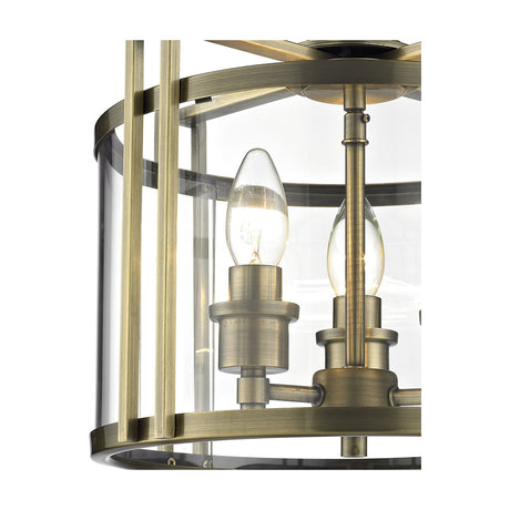 Close-up of the Eaton 3 Light E14 Semi Flush Ceiling Light in antique brass, showing clear glass shade, exposed candle bulbs, and vertical brass frame bars against a white background.