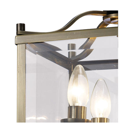 Close-up of the Aston 4 Light Semi Flush Ceiling Light, showing a square clear glass panel in a slim antique brass frame with two lit candle bulbs visible inside.