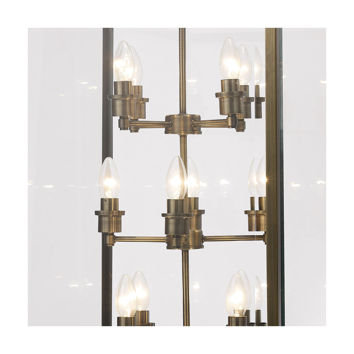 Close-up of the Aston 12 Light E14 pendant light, showing exposed candle bulbs on an antique brass frame with clear glass panel sides against a plain white background.