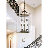 Aston 12 Light E14 Pendant Light in antique brass with a square glass-panelled frame and exposed candle bulbs, hung from a chain above a staircase in a hallway.
