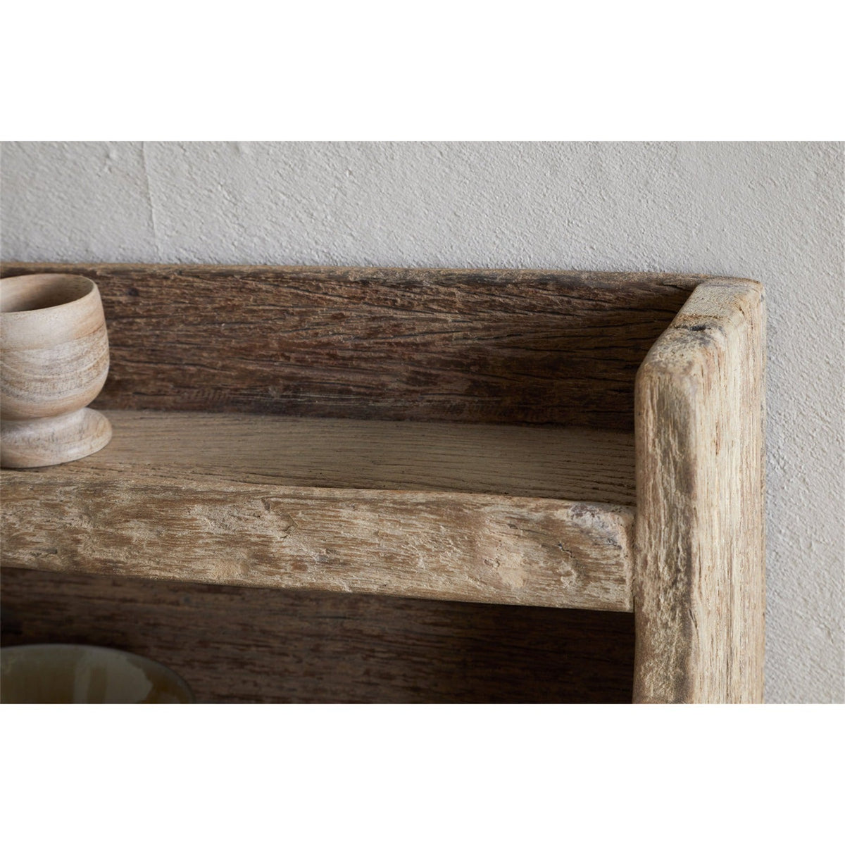 Close-up of the Ibo reclaimed wood wall shelf in natural finish, showing the curved side support and textured grain against a plain wall.