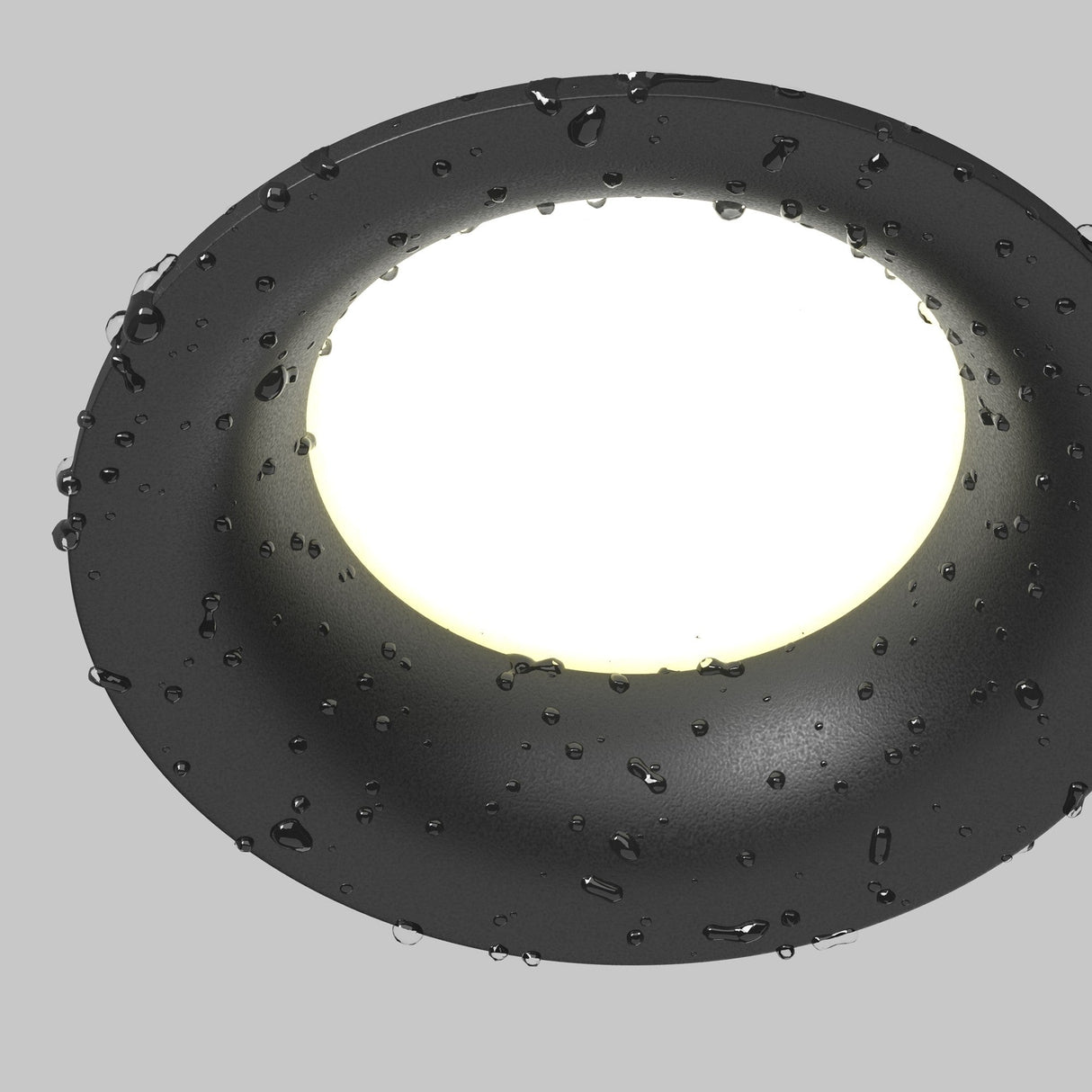 Close-up of the Slim Outdoor Fixed Round Recessed Downlight in black, featuring a minimalist design with water droplets on its illuminated surface against a light grey background. This weather-resistant downlight offers elegant lighting for any setting.