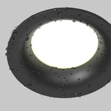 Close-up of the Slim Outdoor Fixed Round Recessed Downlight in black, featuring a minimalist design with water droplets on its illuminated surface against a light grey background. This weather-resistant downlight offers elegant lighting for any setting.