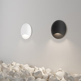 The Biscotti Outdoor 1 Beam LED Recessed Wall Light in white, paired with a black circular light, enhances a minimalist area. Positioned above white stones, they emit a soft, energy-efficient glow onto the smooth, light-colored wall.