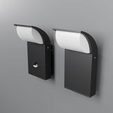 Two Stock Outdoor Motion Sensor LED Wall Lights, finished in graphite with a rectangular base and curved white cover, are positioned side by side against a gray background, combining style with functionality.