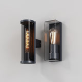 Two modern wall sconces with visible filament bulbs adorn a plain wall. The left, a cylindrical sconce with a spiral filament, is named Conf Outdoor Round Wall Light in graphite. The right is rectangular with a teardrop bulb. Both have sleek dark metal casings and are IP54 protected for modern exterior lighting.
