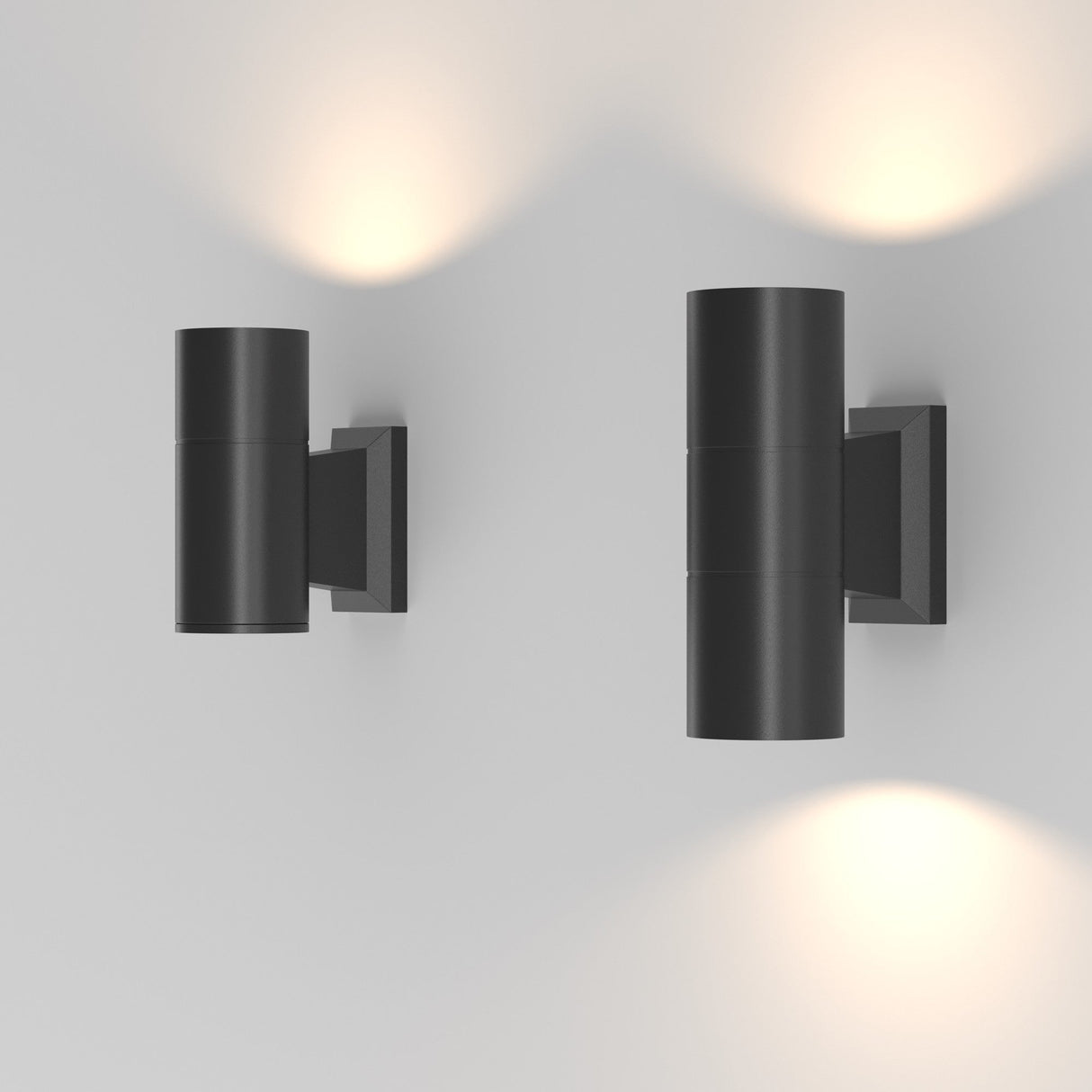 The Bowery Outdoor 1 Light Wall Light in black (O574WL-01B) offers a modern minimalist aesthetic with its cylindrical design. Installed side by side, these IP54-rated lights emit soft, warm light upwards and downwards against a plain white background, ideal for outdoor wall use.