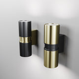 Two Bowery Outdoor 2 Light Wall Lights are mounted side by side; the left is black with gold accents, and the right has a brass finish. Both emit light from both ends and are attached to sleek rectangular wall bases.