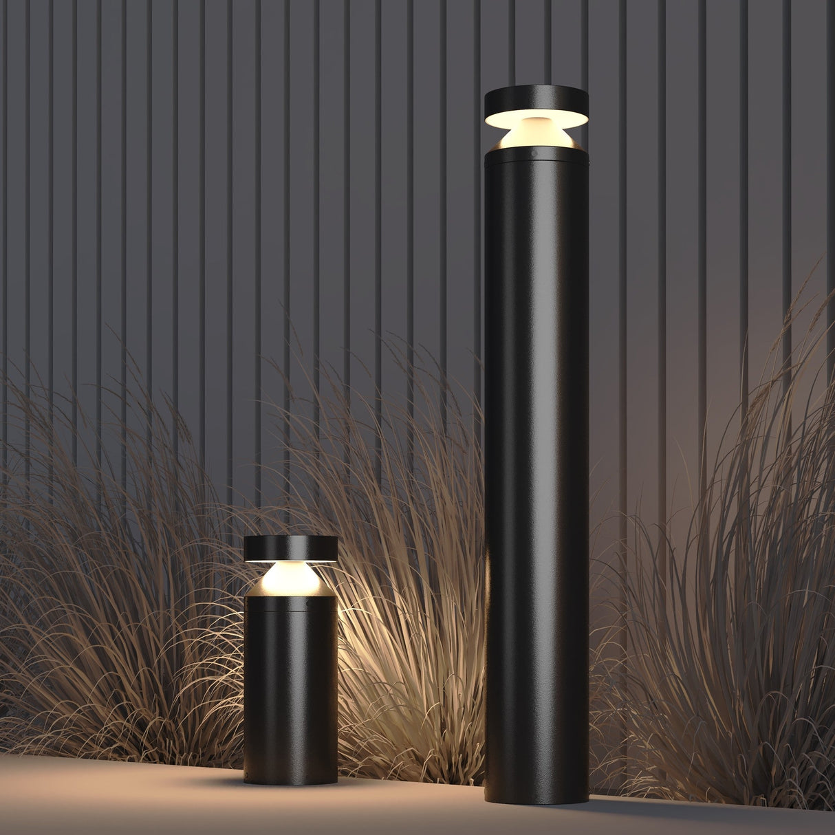 The Olten Bollard Light 30cm - Graphite provides modern outdoor lighting with a sleek, minimalist design. Featuring two graphite cylindrical posts of differing heights, these energy-efficient lights illuminate tall grass against a vertically paneled background.