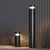 The Olten Bollard Light 30cm - Graphite provides modern outdoor lighting with a sleek, minimalist design. Featuring two graphite cylindrical posts of differing heights, these energy-efficient lights illuminate tall grass against a vertically paneled background.