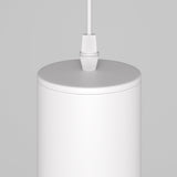 Close-up of the Lipari Short Round Pendant Lamp - White With Gold, a minimalist cylindrical design hanging from the ceiling. Its smooth surface and simple white cord cast a warm glow against a light gray background.