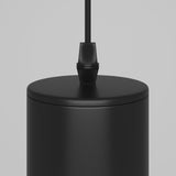 Close-up of the Focus Single Pendant Light - Black, featuring a modern industrial design with a cylindrical black metal finish and an attached black cable, set against a plain gray background.