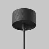 Close-up of the Artisan 1 Light Long Round Pendant in black against a gray backdrop, featuring a textured geometric pattern with an elegant finish and a central rod extending downward.