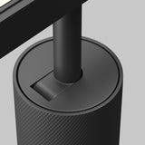 A modern, textured cylindrical stand supports a screen with an anti-glare filter. The sleek, black stand features a geometric design and cable management slot. An Artisan LED Magnetic Exility Track Spotlight 12W 4000K in black highlights the setup against a neutral gray background.