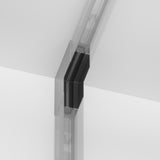 Close-up of a transparent frameless glass door hinge with a minimalist design and the S35 Magnetic Surface-Mounted Track Internal Corner Connector - Black between two glass panels, offering a seamless, modern look against a neutral background.