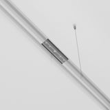 The Exility Magnetic Surface-Mounted Track Straight Connector in black is suspended by two thin cables from the ceiling. With a minimalist, long rectangular design and subtle silver accents, it adds elegance as both a stylish lighting system accessory and a contemporary fixture against the white ceiling.