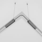 The Exility Track Flexible Corner Power Connector - Black, a modern and sleek pendant light fixture with a bent design, is suspended by two cables in contemporary interiors. It features two linear segments meeting at a right angle and integrates seamlessly with the white ceiling above.