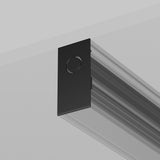 A sleek, black Exility magnetic track end cap is attached to a light gray wall. Its modern design features a minimalist circular detail, similar to track lighting, with the perspective emphasizing its understated elegance as it extends from the wall.