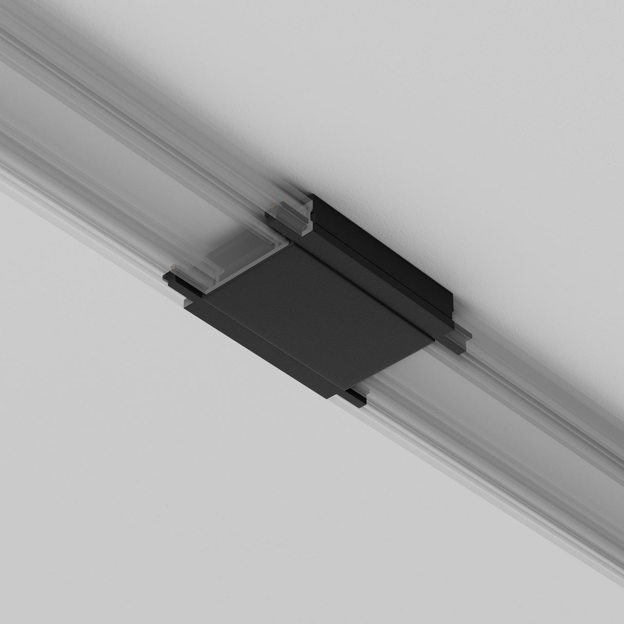 A black rectangular object, likely a Radity Magnetic Track Straight Power Connector - Black, is attached to the ceiling within a linear metallic track. It contrasts against the white ceiling, implying a modern magnetic track lighting or support system.