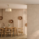A minimalist dining room showcases a wooden table with six chairs. Beige walls hold round, sculptural accents, and the elegant Messina Chandelier - Gold adorns the ceiling. The table is beautifully set with a tea set and a single flower.