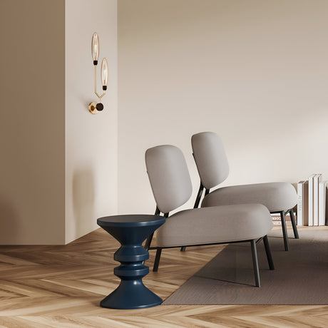 A minimalist room showcases two beige chairs with black legs on a herringbone wood floor, accompanied by a dark blue side table. Ventura 2 Light Wall Lights in gold with amber glass add a modern touch, while a small stack of books lies on the floor by the wall.