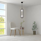 A minimalist room features a beige chair, a small round table with vases of greenery, and a potted plant on the wooden floor. A Ring 2 Light Pendant in black, with white glass spheres, hangs from the ceiling. A large window showcases a green landscape view.