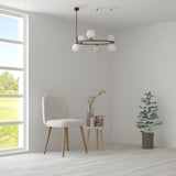 A minimalist room with a white chair and round table exudes modern elegance. Vases and greenery add charm, while the Ring 6 Light Circular Suspension in gold with white glass hangs gracefully. A large window on the left frames a lush green landscape outside.