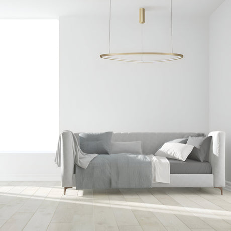 A minimalist living room features a light gray sofa with gray and white cushions and a draped throw against a white wall. The Glint LED Circular Suspension Light 80cm - Brass provides energy-efficient lighting, while the serene space is completed with light wood flooring.
