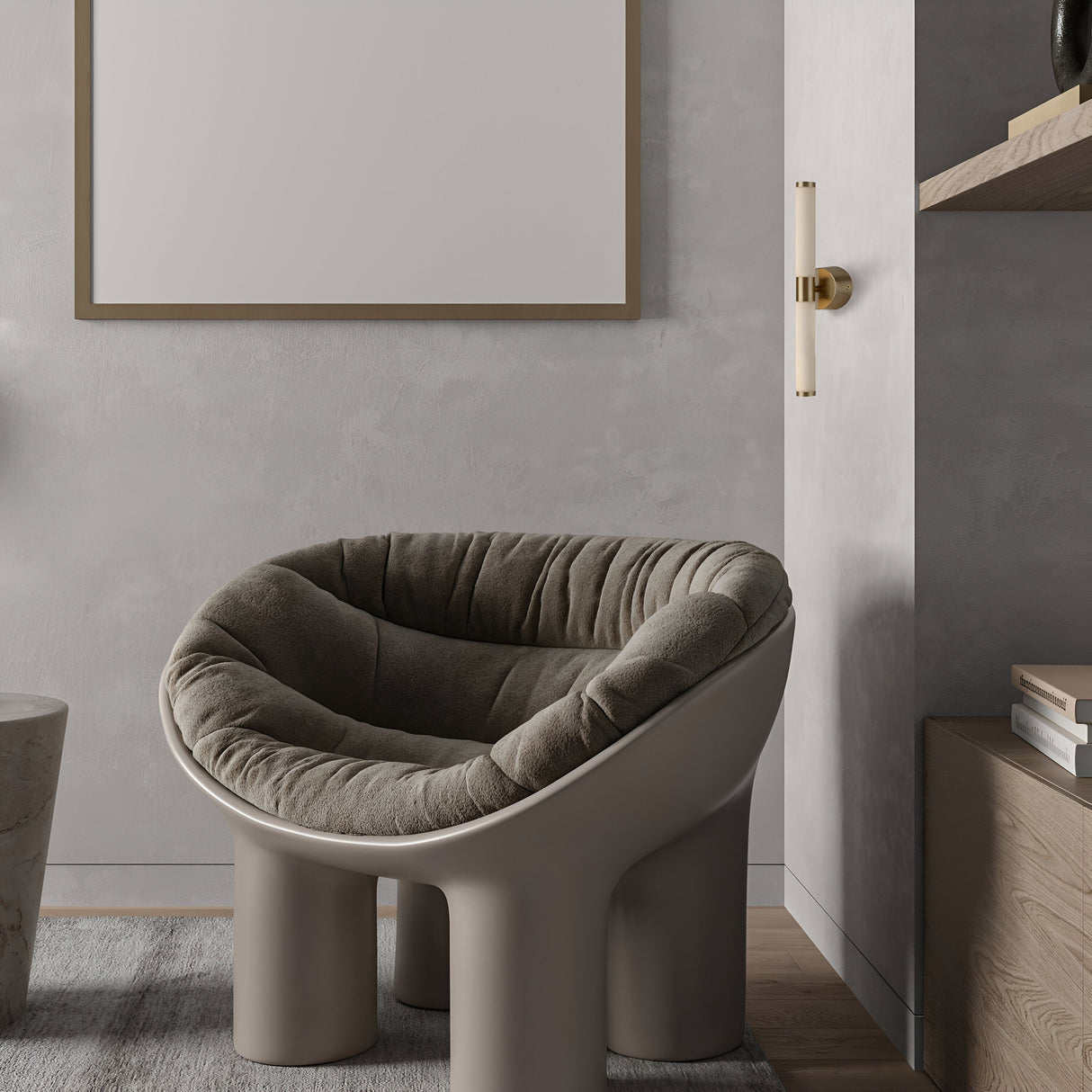 A modern room with minimalist design includes a plush gray curved armchair on a wood floor, next to a small round table. Light gray walls highlight a blank framed canvas and the Axis LED Wall Light 10W 3000K - Gold above the gold-handled door.