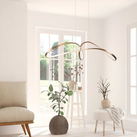 A minimalist, sunlit room boasts the Curve LED Loop Suspension Light in gold with an integrated LED. White walls and large windows enhance the spaciousness, complemented by a beige chair, two potted plants, and a small table with branches on the light wood floor.