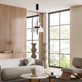 A modern living room with contemporary interiors features minimalist design, a light gray sofa, round marble coffee table, and sleek armchair. Large windows illuminate geometric sculptures and wooden wall paneling, while the Bangkok LED Pendant Light 25cm - Black With Clear Glass Shade hangs above.